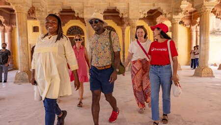 Group of travellers with leader laugh while walking through beautifully carved interior of Amber Fort in Jaipur