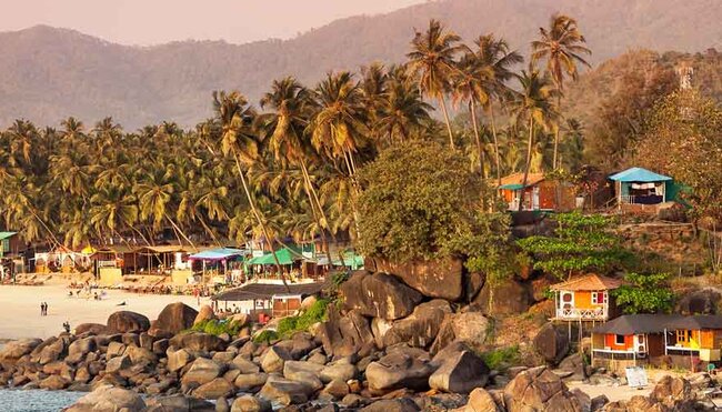 Tropical sunset beach with bungalow and coconut palm trees at Palolem in Goa, India
