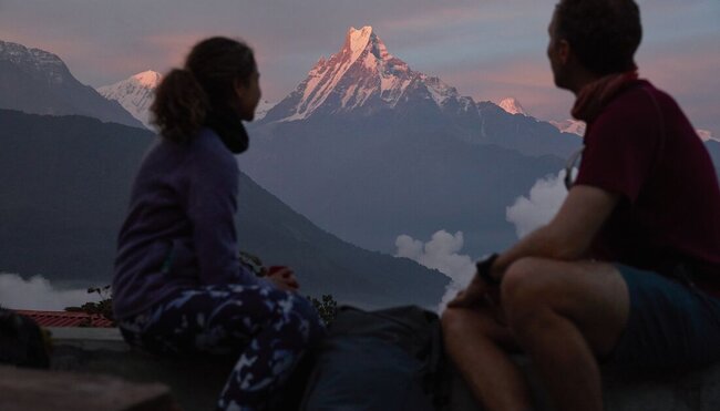 Two travellers look out from a lodge as sunrise hits a mountain in Annapurna morning in Nepal