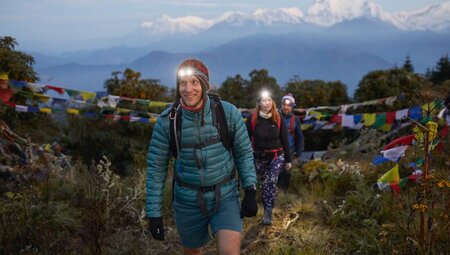 Travellers wearing headlamps and backpacks hike toward a hilltop for a spectacular sunset view in Nepal