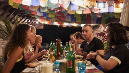 Travellers talk smile and laugh over dinner in Pokhara with prayer flags overhead in Nepal