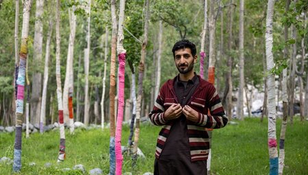 Local from Yugo village stands in front of birch trees with knitted covers to keep goats from eating bark
