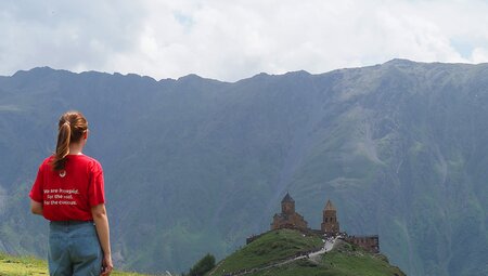 Intrepid leader stands at the crest of a hill looking out at the Gergeti Trinity Church with Mount Kazbek behind it in Georgia