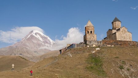 Intrepid travellers approach the Gergeti Trinity Church after a steep climb, with Mount Kazbek visible behnd