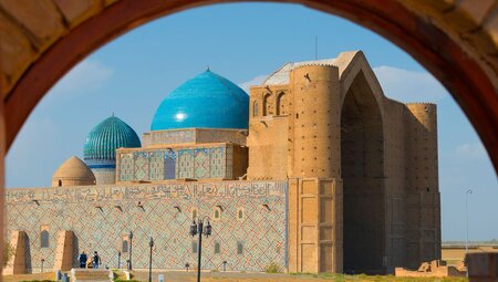 The cerulean domes of  Khoja Ahmed Yasawi Mausoleum visible through a sandstone arch, Turkistan, Khazakhstan