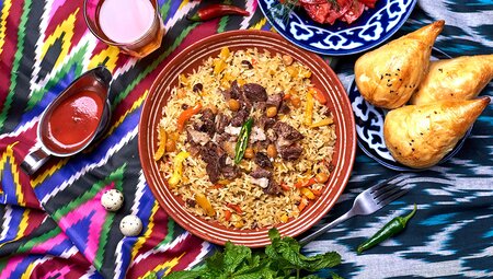 Traditional Uzbekistani plov with samsa, juice, chili and salad