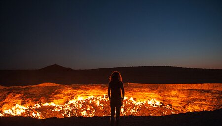 Intrepid Traveller stands before the constantly burning crater of Darvaza at night in Turkmenistan