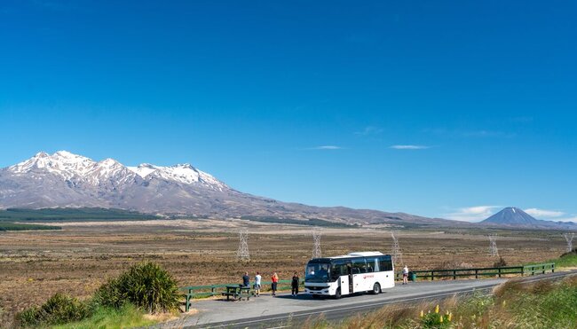 Travellers' tour bus pulled over on side of road so travellers can enjoy the view of Mount Tongariro, New Zealand