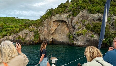 Travellers on a boat ride, viewing the Maori artwork on carved into the cliffside at Lake Taupo, New Zealand