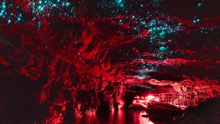 The Waitomo glow worm caves being illuminated red as travellers explore via a raft in New Zealand