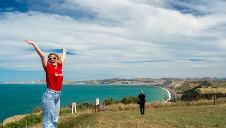 Leader throwing her hands up with a scenic coastal view behind her at Marlborough Sounds, New Zealand