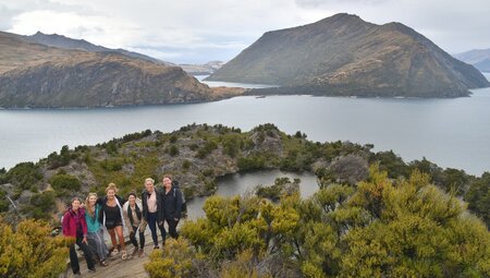 Group of travellers standing on a hill with the beautiful Lake Wanaka in the background in Wanaka, South Island, New Zealand