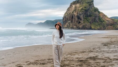 Traveller walking down Piha Beach with Lion Rock in the background in Auckland, New Zealand