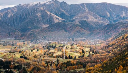 Aerial view of Arrowtown, warm autumn colours and mountainscape in the background