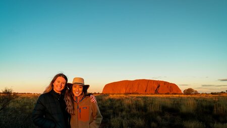 Intrepid travellers pose for a happy photo with Uluru hit by the sunset beyond