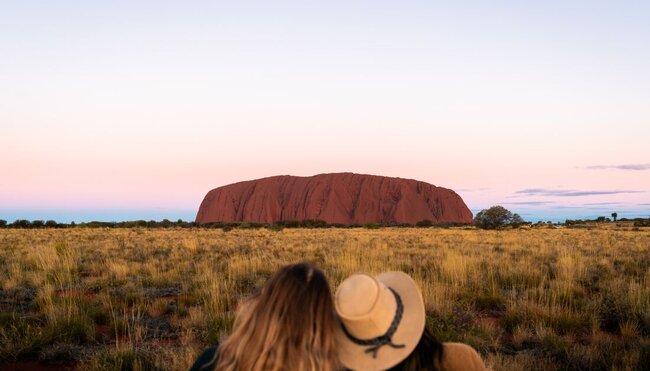 Two Intrepid travellers lean on each other looking out at Uluru in Australia's Red Centre