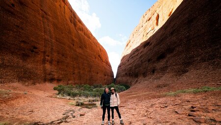 Two travellers pose happily between sweeping stone sides of Kata Tjuta in the Red Centre of Australia