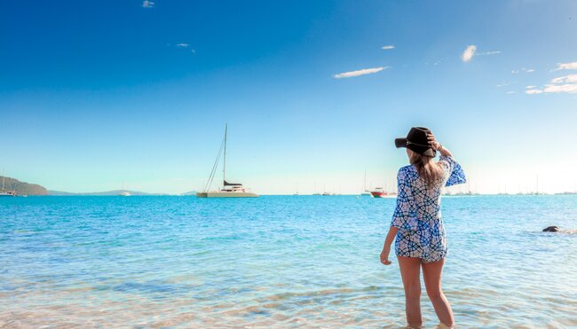 18 to 35s travellers looks out over Whitsunday Island beach with boats anchored off shore