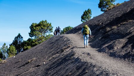 Intrepid travellers on a volcanic rock ridge with backpacks hike up the slopes of Acatenango in Guatemala