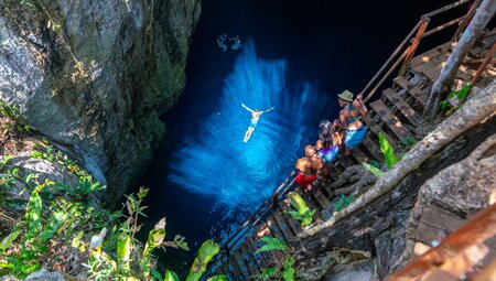 Intrepid travellers watch another swimmer in the reflective crystal blue waters of one of Mexico's cenotes