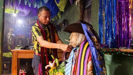 Guatemalan local affixes fabric to a statue of San Simon in an Atitlan home smoking ceremony
