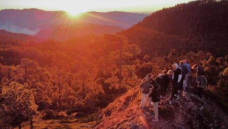 Travellers stand on a ridge looking out as dawn rises over the mountains and forests of rural Oaxaca in Mexico