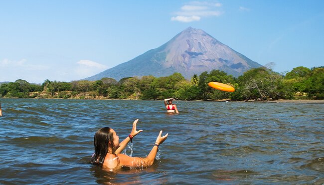 Friends play frisbee in the water in the shadow of volcano Concepcion, Ometepe island, Nicaragua