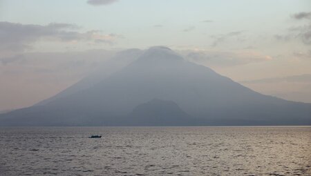Calm Lake Atitlan with boat on the water and volcano in the background on a misty morning, Guatemala