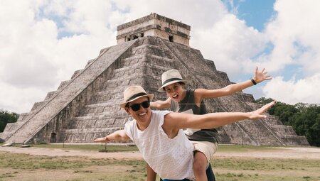 Happy mother and daughter with arms stretched out openly in front of El Castillo, Chichen Itza, Yucatán, Mexico
