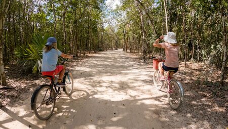 Travellers cycling on dirt path surrounded by trees in Mayan City, Coba, Mexico