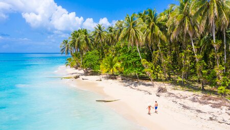 Bocas del Toro beach seen from a drone view with two travellers in swimwear walking down the beach