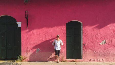 Traveller leans against a bright pink painted building in the streets of Suchitoto in El Salvador
