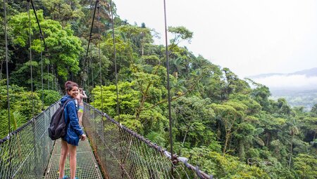 Traveller crosses the Arenal bridge amongst the tree tops in Costa Rica
