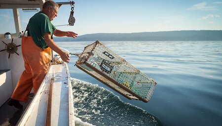 Lobster boat fisherman throwing a lobster trap into the ocean off the shore of Canada's Maritimes