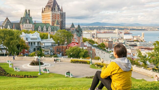 Travelling sitting on green grass, admiring the view of Chateau Frontenac Castle at Old Quebec, Canada