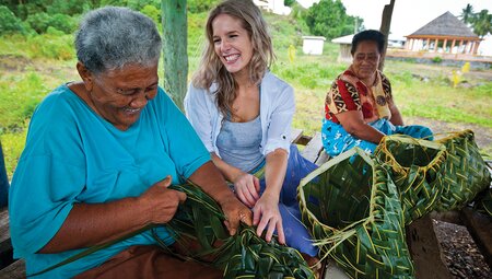 Customer learning to weave baskets the Samoan way (Fa'a) with two smiling locals