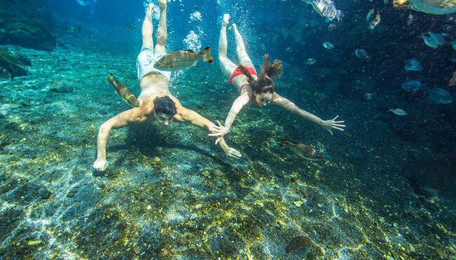 Two passengers swimming in a crystal clear cave pool in Samoa