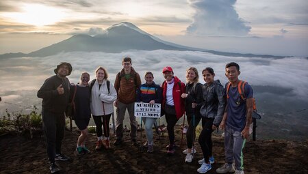 Travellers pose for a photo at the lookout of the Mount Batur Sunrise Hike with morning mist and distant mountains in the background in Bali