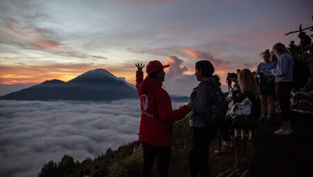 Leader with travellers enjoying the view of a glowing sunrise during the Mount Batur hike, Bali, Indonesia
