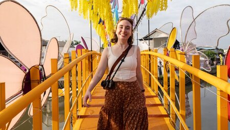 Smiling traveller walks on a yellow bridge over a canal in Chiang Mai, Thailand