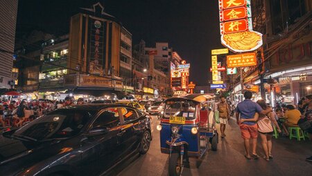 Tuk tuk and cars on the rooad and people filling the streets at night in Bangkok.