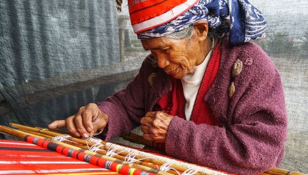 Elderly Ifugao woman weaving with loom in traditional clothes and hat