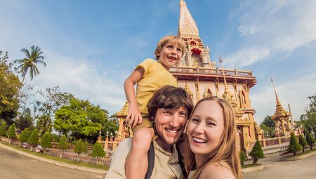 Family with parents and child pose happily for a photo in front of Wat Chalong Temple in Phuket