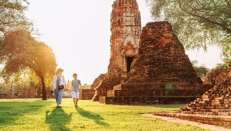 Mother and son walk through Wat Phra Mahathat temple in Atutthaya as sun shines through background