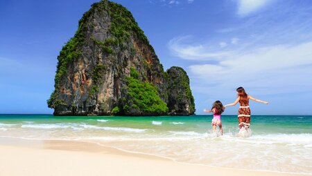 Mother and daughter laugh with joy run into the surf at Railay beach in Krabi Thailand