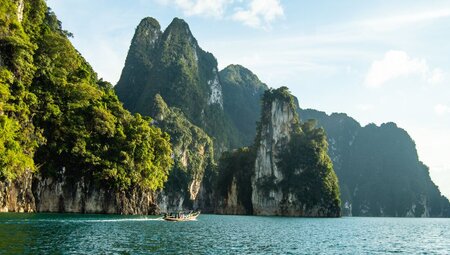 Longtail boat floats past huge limestone mountains in Khao Sok National Park in Thailand