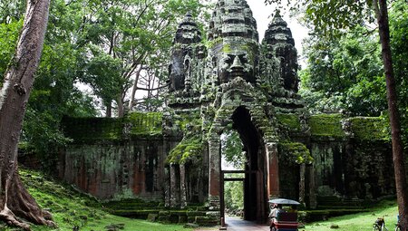 Travellers arriving by tuk-tuk to the entrance of a temple in the Angkor region in Cambodia.