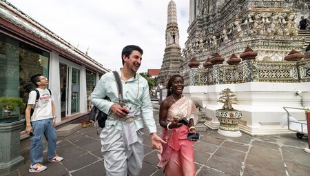 Two laughing travellers dressed in traditional Thai attire at Wat Arun, Bangkok, Thailand