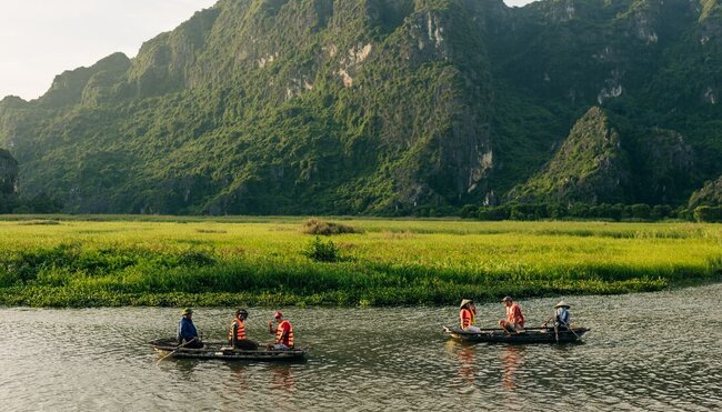 Wide shot of travellers and leader being guided on rowboats in the wide river valley of Van Long Nature Reserve