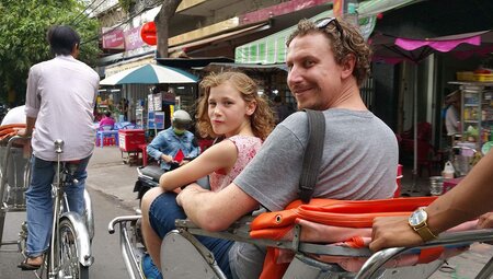 Father and daughter travelling on a rickshaw down a busy Hanoi street on an Intrepid Travel tour.